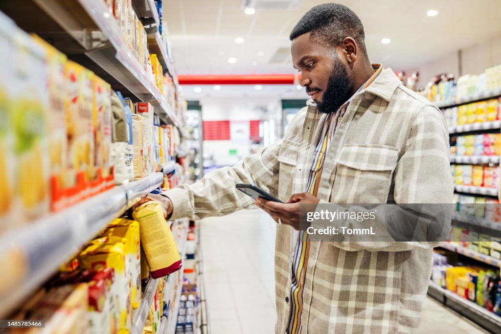 Man Looking At Smartphone While Choosing Items In Supermarket
