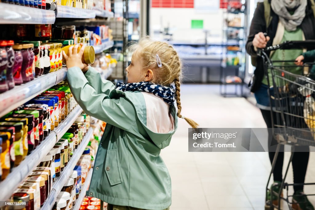 Une jeune fille tend la main pour regarder un produit sur les étagères d’un supermarché
