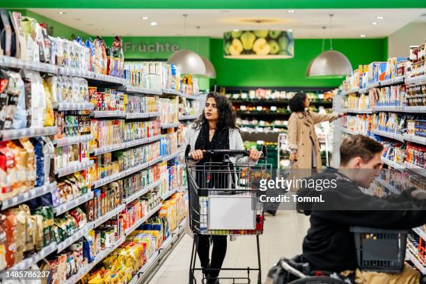 frau schiebt einkaufswagen den gang hinunter, während sie supermarktprodukte durchstöbert - supermarket trolley female stock-fotos und bilder