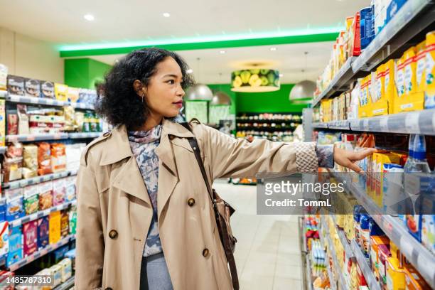 donna che raggiunge l'articolo durante la navigazione dei prodotti del supermercato - pick foto e immagini stock