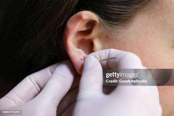 young woman puncturing her ear - pierced stockfoto's en -beelden