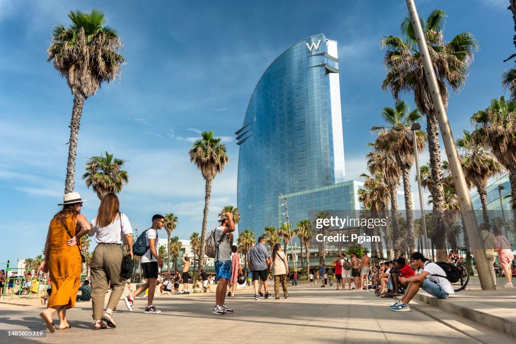 A crowd of people walk along the boardwalk of Barceloneta Beach in Barcelona Spain