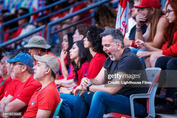 older adult male in crowd of fans yawns and checks the time on his watch during big soccer match - recreational sports league stock pictures, royalty-free photos & images