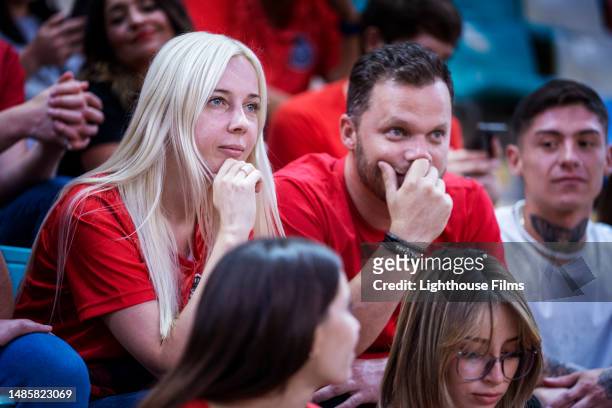 couple sits in bleachers on the edge of their seats with anticipation during a sports game - heteroseksueel koppel stockfoto's en -beelden