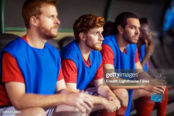 international football players on reserve sit and watch their teammates play in a critical soccer match - reserve athlete stock-fotos und bilder