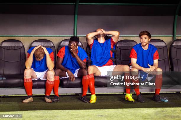 benched professional soccer players sit with their head in their hands while watching their teammates lose - side lines photos et images de collection