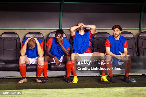 Benched professional soccer players sit with their head in their hands while watching their teammates lose Benched professional soccer players sit with their head in their hands while watching their teammates lose