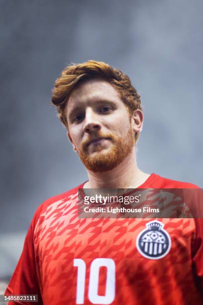 portrait of an adult male professional soccer player with red hair looking at a camera with fog behind him - midfielder soccer player stockfoto's en -beelden