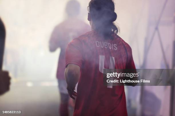 an adult male professional soccer player jogs through a fog-filled tunnel onto a large stadium for a crucial game - football running back stock pictures, royalty-free photos & images