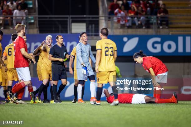 soccer teams chaotically argue with referee during a game over a penalty yellow card as one player lays down on a stadium field - referee card stock pictures, royalty-free photos & images