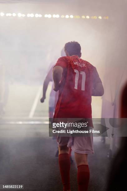 a professional male soccer player jogs through a magnificent fog-filled tunnel onto a stadium field - football player tunnel stock pictures, royalty-free photos & images