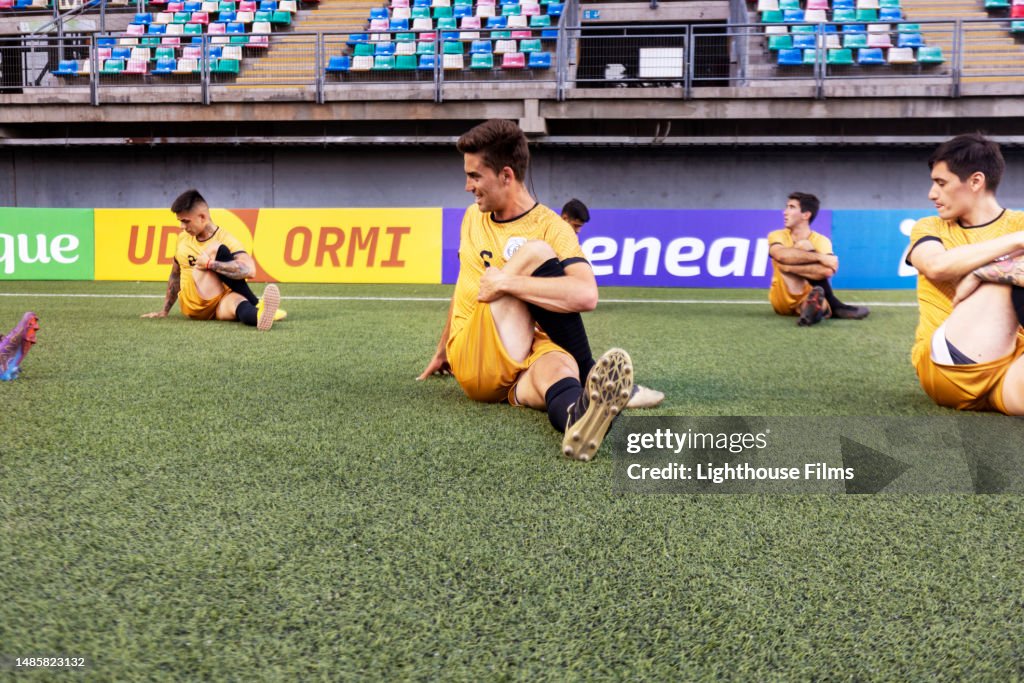 Focused professional soccer players stretch during warm-up exercises on stadium field before game begins