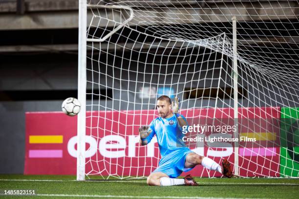 agile male soccer goalie dives to block shot headed toward his goal in an intense international match - pre positioned stock pictures, royalty-free photos & images