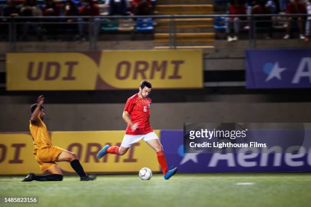 an international football player kicks soccer ball up field as opponent slides in and attempts to steal it - försvarare fotbollsspelare bildbanksfoton och bilder