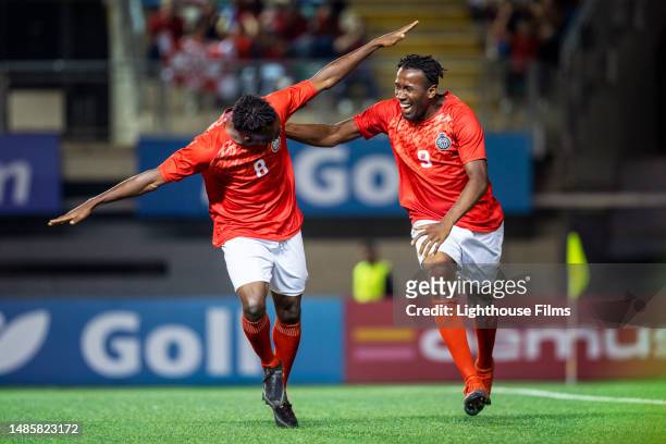 two professional male soccer players excitedly celebrate by embracing and running with arms out after scoring a goal - two guys playing soccer stockfoto's en -beelden