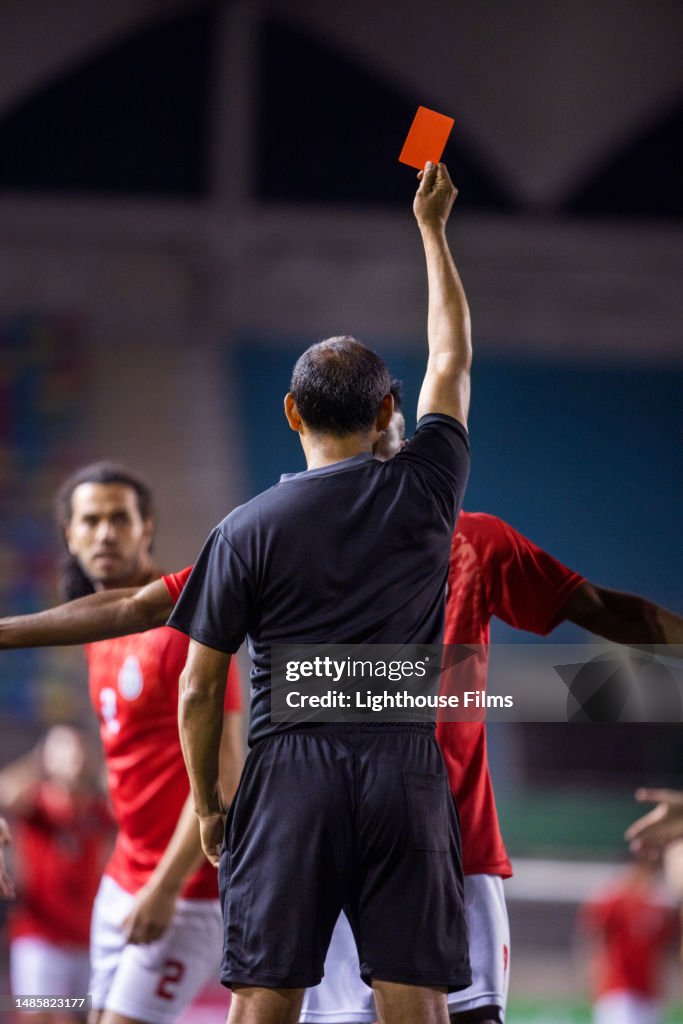 Rearview shot of professional referee lifting a red card up to penalize soccer player