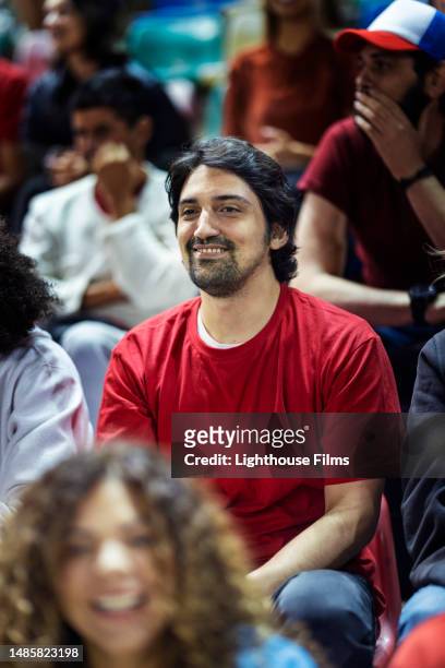 adult male sports fan sits happily in a large crowd of supporters to watch his favorite soccer team play - bleachers stock pictures, royalty-free photos & images