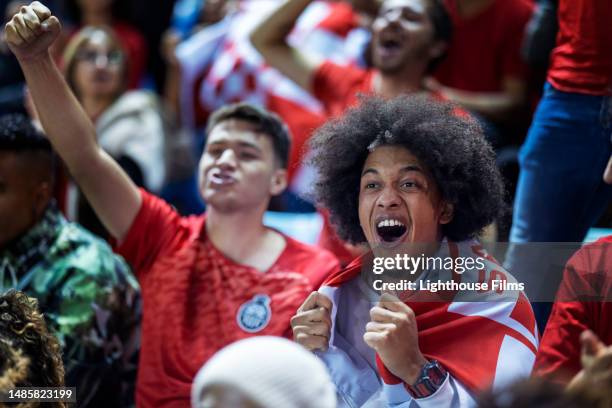 delighted loyal soccer fans excitedly cheer while sitting in stadium bleachers after their favorite team scores - football fan stock pictures, royalty-free photos & images