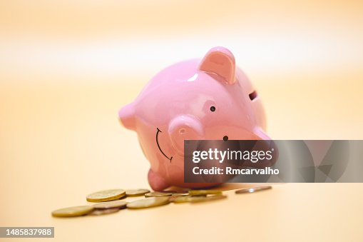 A piggy bank lying with coins in studio shot. Orange background. A piggy bank lying with coins in studio shot. Orange background.