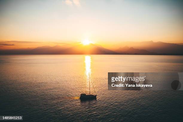 a cinematic landscape with a luxury yacht gliding on the still sea surface in the orange sunset - sunset society stock-fotos und bilder