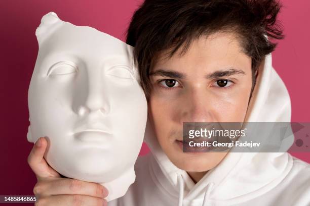 portrait of a suspicious young man in white hoodie covering face with a mask. secret admirer, hidden identity concept. isolated on pink background. - pink colour scheme stock pictures, royalty-free photos & images