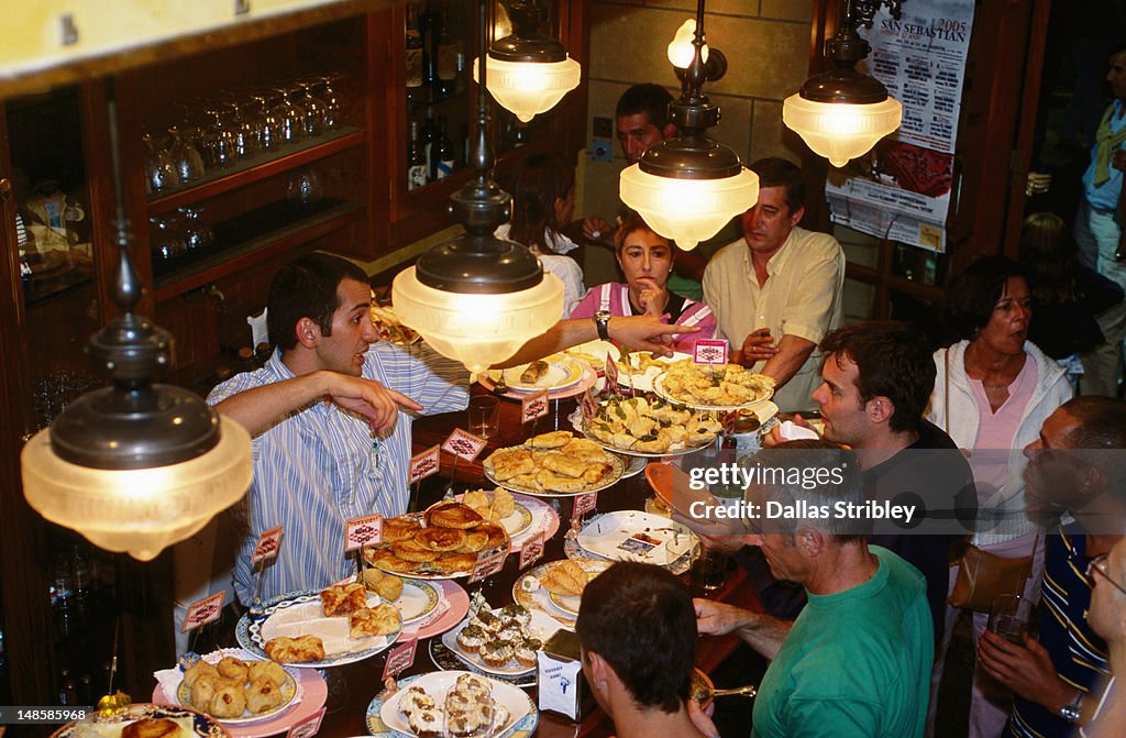 People dining at Pintxos line counter of busy "Ormazabal Tabema" bar.