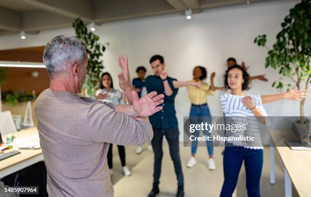 man leading a group of workers stretching on an active break at the office - staff wellbeing stock pictures, royalty-free photos & images