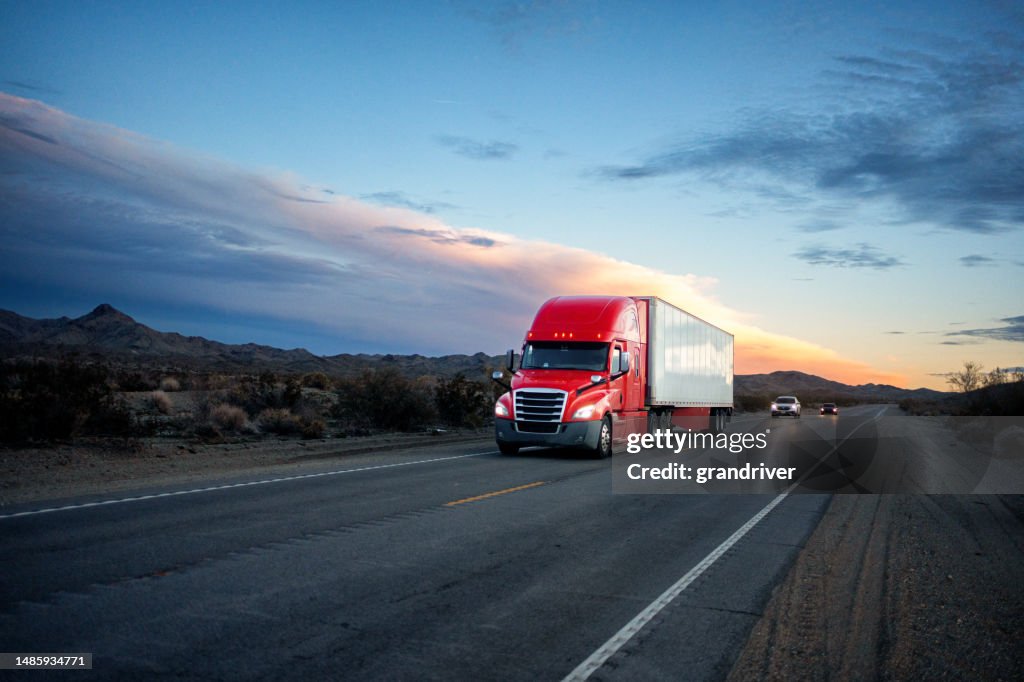 Roter Sattelschlepper fährt bei Sonnenuntergang eine zweispurige Autobahn in der abgelegenen Wüste von Arizona entlang und wirft eine dramatische Silhouette gegen den leuchtenden Himmel