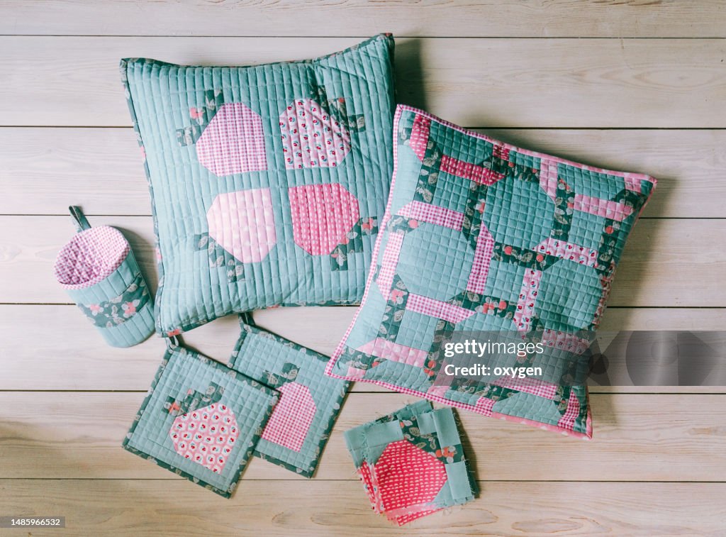Patchwork Aqua Pillows witch Chain of Pink and Green color and strawberry Block Shape on a Wooden Logs. Scandinavian Hugge Style. Needlework and Quilting