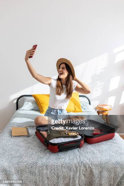 cheerful young adult pretty woman taking selfie portrait with mobile phone while preparing her travel suitcase before going on summer vacation. - holiday preparation stock pictures, royalty-free photos & images