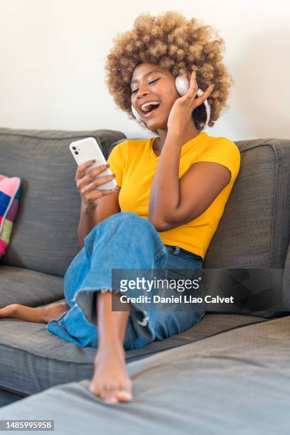 young woman dancing and singing on the sofa at home - auriculares stock pictures, royalty-free photos & images