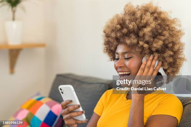 close-up of a young afro-caribbean woman enjoying music on the sofa - auriculares stock pictures, royalty-free photos & images