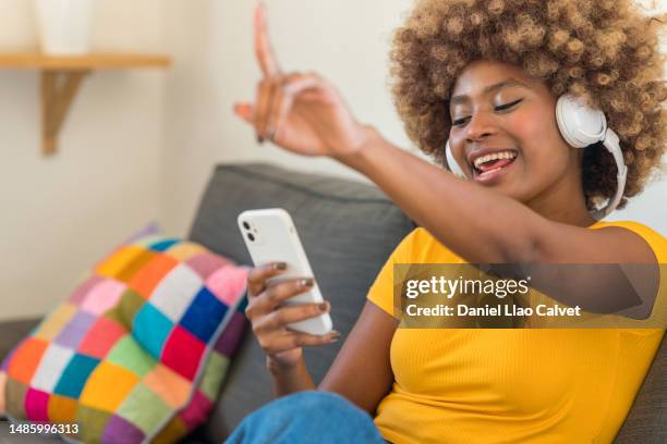 close-up of a young woman sitting on the couch enjoying music - auriculares stock pictures, royalty-free photos & images