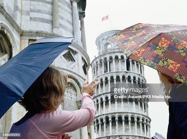 women with umbrellas looking at leaning tower of pisa. - pisa study stock-fotos und bilder