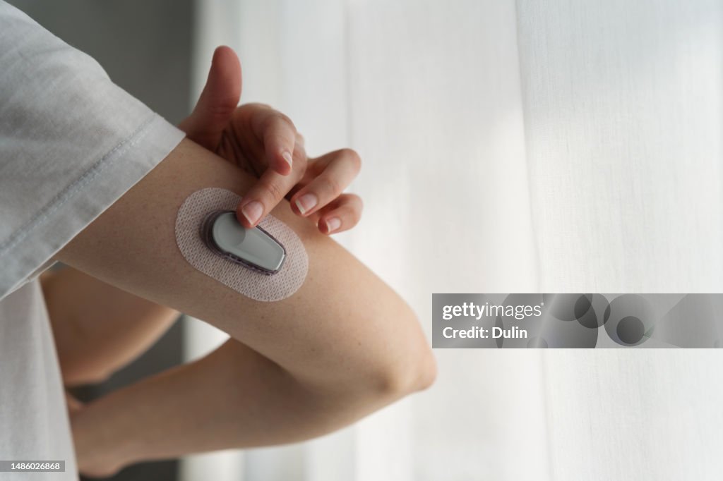 Close-up of a woman attaching a continuous glucose monitor to her arm