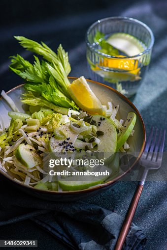 Bowl of celery salad with apples and sesame seeds with a glass of water with apple, celery and lemon Bowl of celery salad with apples and sesame seeds with a glass of water with apple, celery and lemon
