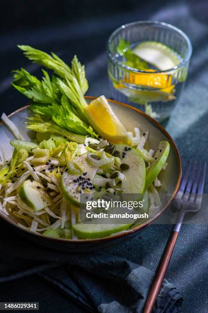 bowl of celery salad with apples and sesame seeds with a glass of water with apple, celery and lemon - food design stock pictures, royalty-free photos & images