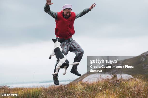 dog and person jump for joy as they play on hillside island - kindness stock pictures, royalty-free photos & images