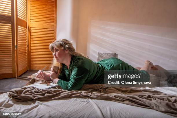 full-figured woman writes in her diary in the morning on the bed - thick white women fotografías e imágenes de stock