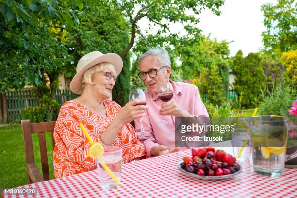 älteres paar stößt weingläser an, während es am esstisch im garten sitzt - kirschen tisch weiß stock-fotos und bilder