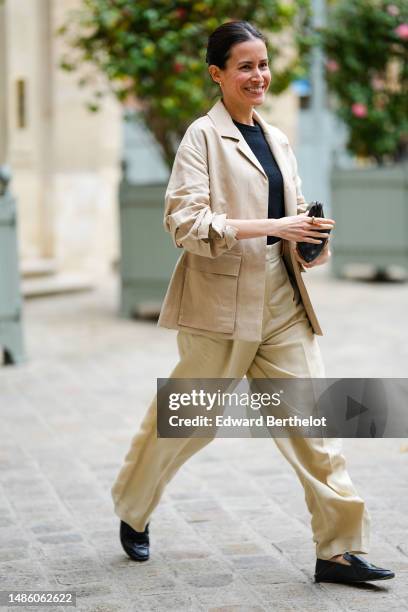 Guest wears a black t-shirt, a beige blazer jacket, pale yellow large suit pants, black shiny leather loafers , a black shiny leather clutch ,...