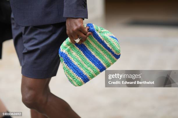 Guest wears a navy blue blazer jacket, matching navy blue suit shorts, a royal blue / beige / green striped print pattern braided wicker clutch ,...