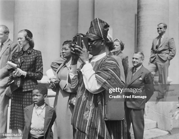 Man takes pictures of guests arriving for the wedding of Lady Peggy Cripps and Joseph Appiah at St John's Wood Church in London in June 1953. Lady...