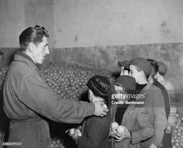 Man hands oranges to Italian children at a camp for displaced persons set up by the Allied Military Government in Florence, 1945. The children are...
