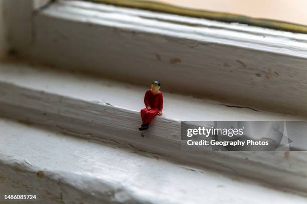 Small plastic figure of man in red clothes placed in window frame.