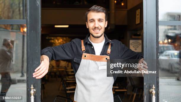 smiling barista man opening morning coffee shop doors - white apron stock pictures, royalty-free photos & images