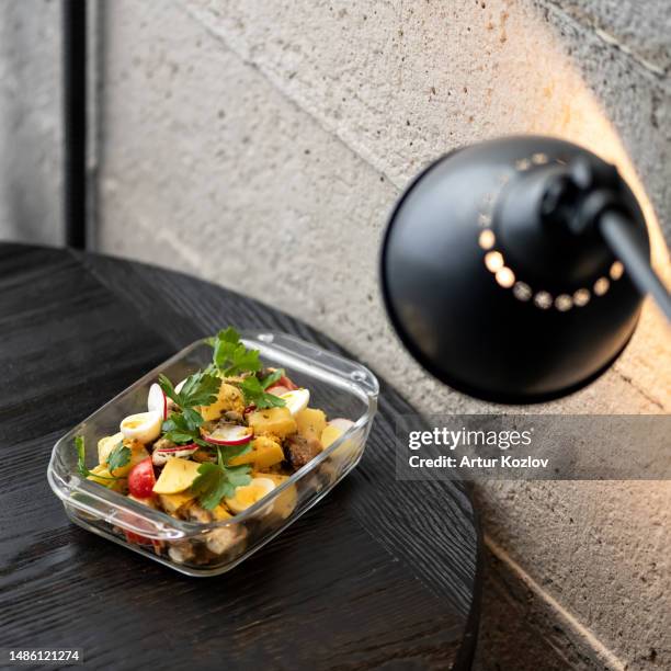 salad with potatoes, meat, egg and radish in transparent bowl on table. dish on dark gray wooden table under table lamp. dark gray background. view from above. copy space - darkwood beach foto e immagini stock