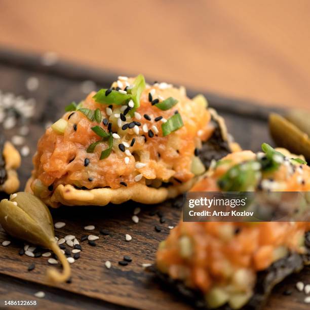 snacks with red fish paste are decorated with green onions and sesame seeds on wooden board. cold appetizers. sandwiches with salmon. side view. soft focus. close-up - terrine photos et images de collection