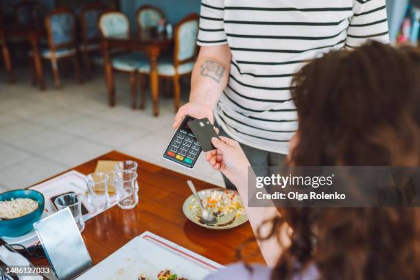nfc technology in cafe. unrecognizable woman customer paying by card in restaurant, sit at wooden table - tap card stock pictures, royalty-free photos & images
