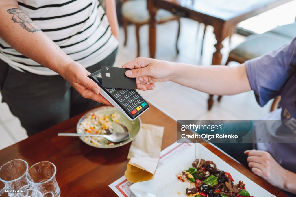 Contactless payment in restaurant. Wireless card reader scanning credit card from customer hand in cafe, high angle view